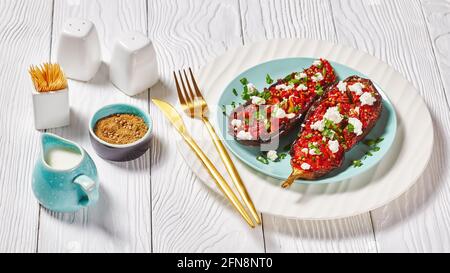 Imam Bayildi con Feta sbriciolato, melanzane farcite con pomodori salati, cipolle e spezie su un piatto su un tavolo di legno bianco Foto Stock