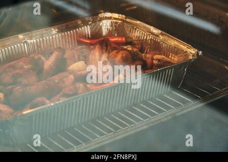 Le ali di pollo in marinata vengono cotte in alluminio nel forno. La foto è stata scattata attraverso il bicchiere del forno. Foto Stock