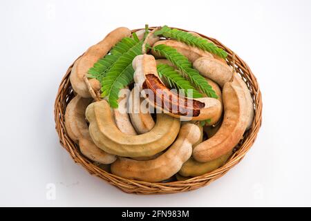 Tamarind  fagiolo come cialde riempite di semi circondati da una polpa fibrosa disposta in un cesto con fondo testurizzato bianco. Foto Stock