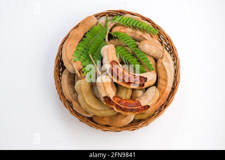 Tamarind  fagiolo come cialde riempite di semi circondati da una polpa fibrosa disposta in un cesto con fondo testurizzato bianco. Foto Stock