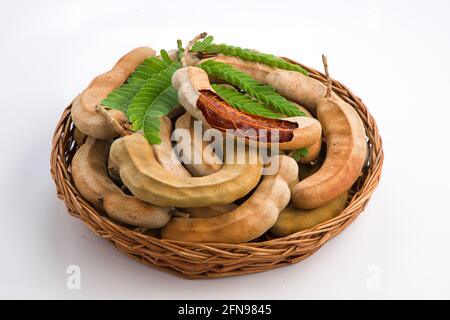 Tamarind  fagiolo come cialde riempite di semi circondati da una polpa fibrosa disposta in un cesto con fondo testurizzato bianco. Foto Stock