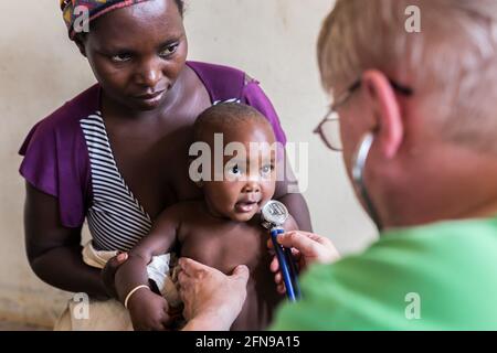 Un medico straniero sta esaminando un bambino in una clinica medica a Mbale, Uganda orientale rurale Foto Stock