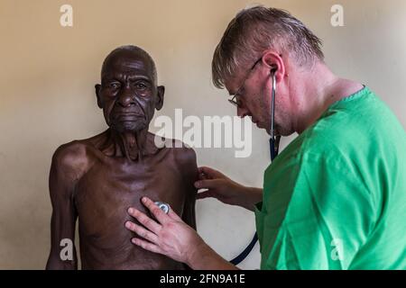 Un medico straniero sta esaminando un anziano in una clinica medica a Mbale, Uganda orientale rurale Foto Stock