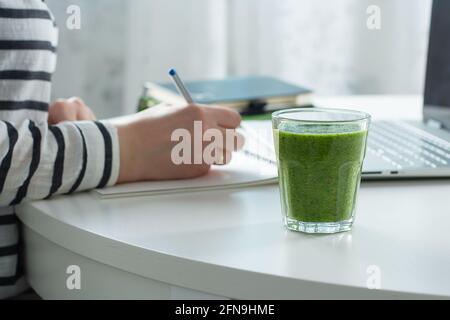 Donna che scrive su notebook e computer portatile nelle vicinanze. Smoothie verde sano fromSpinach, kiwi e mele Foto Stock