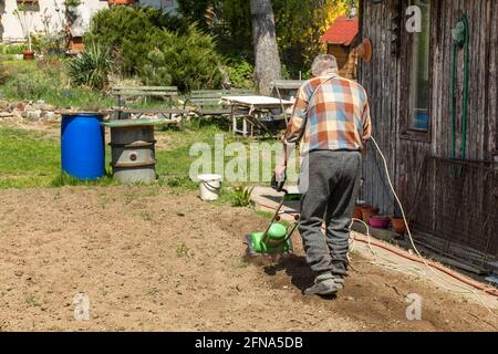 Giardinaggio. Lavori di primavera in azienda. Coltivazione del terreno con un coltivatore elettrico. L'uomo aratura la terra con un coltivatore elettrico. Foto Stock