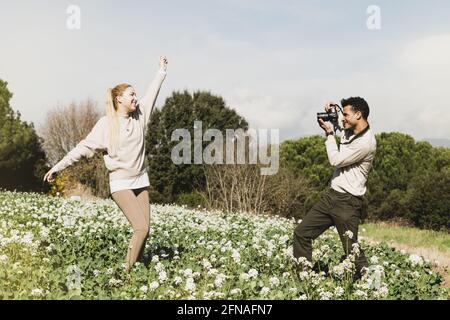 Giovane uomo che scatta le foto della sua fidanzata in piedi tra campo con bracci sollevati Foto Stock