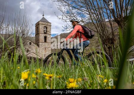 Donna in bicicletta e chiesa romanica di Sant Feliu, Barruera, Vall de Boí, Lleida, Catalogna, Spagna Foto Stock