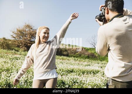 Giovane uomo che scatta le foto della sua fidanzata in piedi tra campo con bracci sollevati Foto Stock