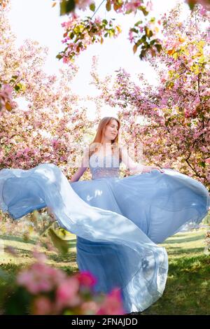 Giovane donna in un vestito blu su uno sfondo di fioritura sakura. Foto Stock