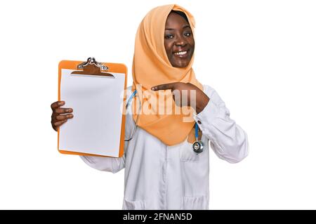 Bella giovane donna africana che indossa stetoscopio medico tenendo appunti sorridente buon puntamento con mano e dito Foto Stock