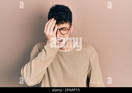 Giovane uomo ispanico che indossa abiti casual e occhiali che sbadano stanco coprendo metà faccia, occhio e bocca con la mano. Faccia fa male. Foto Stock