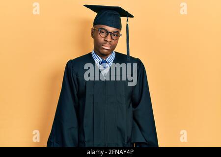 Giovane uomo afroamericano che indossa il cappuccio di graduazione e la cerimonia roboscia osservante sonnolento e stanco, esausto per stanchezza e sbornia, occhi pigri nella mor Foto Stock
