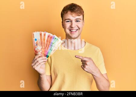 Giovane uomo caucasico che tiene le banconote di peso filippino sorridente che indica felice con mano e dito Foto Stock