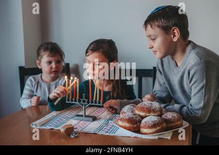 Fratelli e sorelle fratelli che illuminano le candele sulla menorah per la vacanza ebraica Hanukkah a casa. I bambini celebrano il festival di luce di Chanukah. Sognare Foto Stock