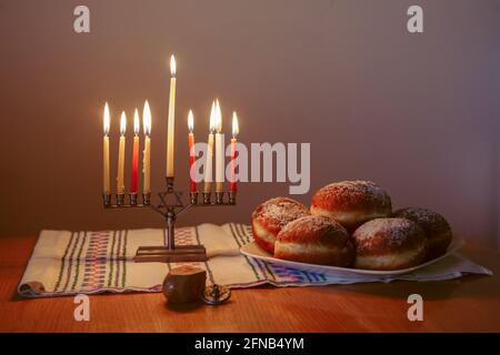 Menorah con candele accese per la vacanza ebraica Hanukkah sul tavolo a casa. Festa delle luci di Chanukah. Dreidel e Sufganiyot ciambelle Foto Stock