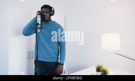 Uomo che indossa le cuffie che canta una canzone in un microfono in uno studio di registrazione. Foto di alta qualità Foto Stock