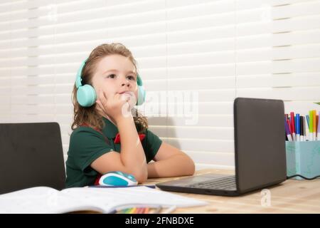 Concetto di scuola domestica. Ragazzo della scuola in cuffia che guarda la lezione online sul computer portatile. Foto Stock