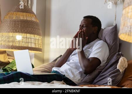 Uomo africano stanco che urla a casa a letto. Foto Stock
