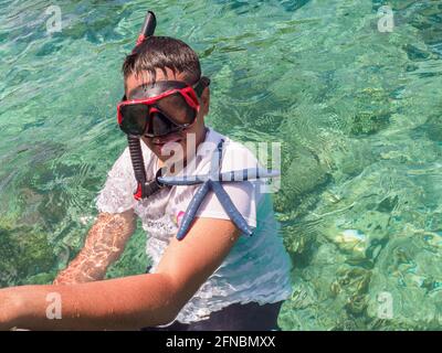 Boy snorkeling nel mare turchese e tenere stelle marine blu, sette isole, isola Seram, Indonesia, Asia Foto Stock