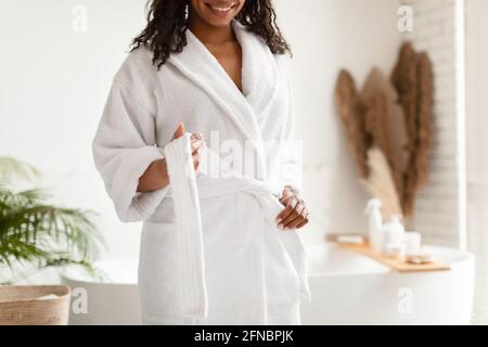 Irriconoscibile African American Lady svincolare accappatoio bianco in piedi in bagno Foto Stock