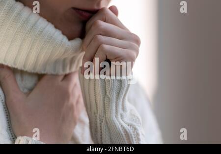 Una donna che tocca la gola con tosse e dolore. Donna malata con influenza in maglione bianco in giorno d'inverno. Foto Stock