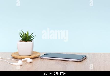 Posto di lavoro in ufficio, scrivania con telefono cellulare, cuffie, impianto domestico. Interno con parete blu, tavolo marrone. Immagine concettuale. Foto Stock