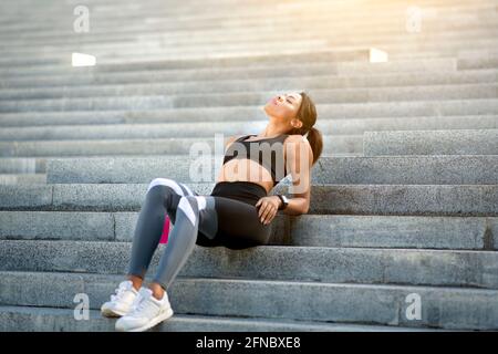 Gioiosa donna sportiva che riposa al parco dopo aver fatto jogging Foto Stock