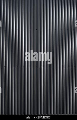 Lamiera di ferro corrugata nera utilizzata come facciata di un magazzino o di una fabbrica. Struttura di una facciata in lamiera di zinco ondulata senza cuciture in alluminio Foto Stock