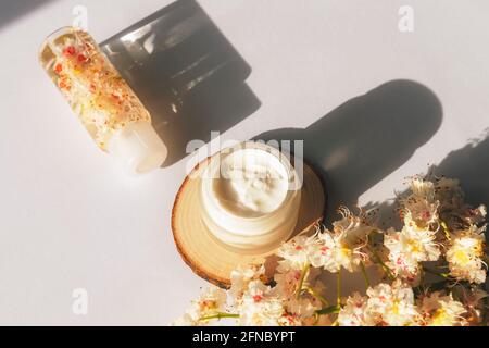 Vasetto di crema e fiori di castagno di Cavallo su tavola bianca alla luce del sole. Concetto di cosmetica biologica naturale. Lunghe ombre dure, vista dall'alto. Foto Stock