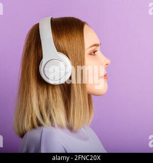 Giovane donna in cuffia ritratto guardando il lato. Donna bella e sicura con ritratto biondo e acconciatura goditi la musica delle canzoni in cuffia Foto Stock