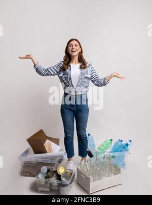 Smistamento rifiuti. Millennial Lady in piedi tra contenitori con diversi materiali per il riciclaggio Foto Stock