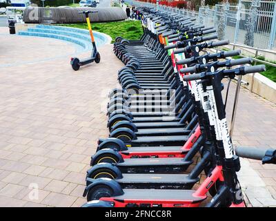 Russia, Sochi 16.04.2021. Ci sono molti scooter elettrici allineati in fila di lastre di pavimentazione. Noleggio scooter Foto Stock
