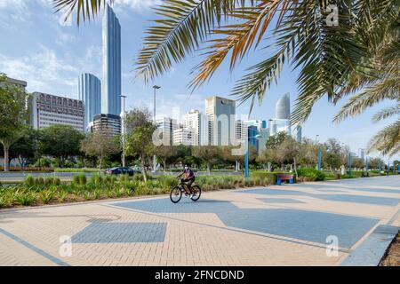 ABU DHABI, Emirati Arabi Uniti - 30 APRILE 2021: L'uomo in bicicletta sulla Corniche di Abu Dhabi al mattino con il paesaggio urbano moderno sullo sfondo. Stile di vita attivo. Foto Stock