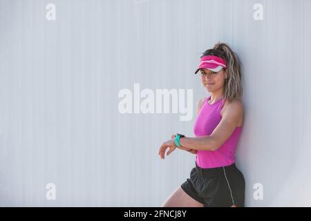 Giovane donna attiva che sta impostando il suo cronometro prima di correre dentro la città in una giornata di sole Foto Stock