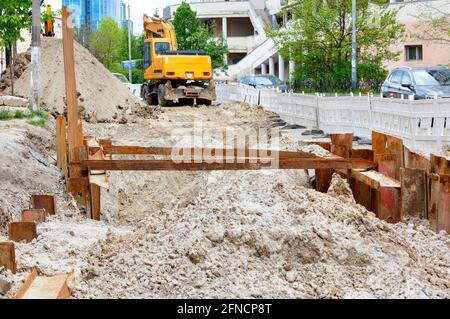 Riparazione di una rete di riscaldamento urbano, sullo sfondo un escavatore di servizio stradale scavava una trincea sulla carreggiata. Foto Stock