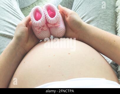 Closeup di donna incinta che tiene i boeties rosa del bambino sul suo ventre. Foto Stock