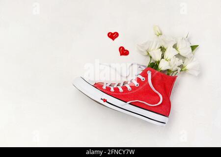 Composizione creativa con sneakers rosse e fiori su sfondo bianco Foto Stock
