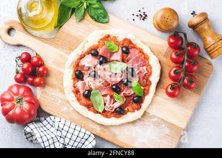 Pizza non cotte con salsa di pomodoro, prosciutto e olive su sfondo ligneo, vista dall'alto. Cottura della pizza a casa Foto Stock