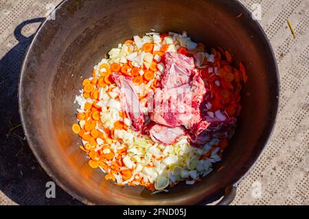 Vista dall'alto su carne cruda e verdure fresche tritate in un vecchio calderone, preparato per cucinare lo stufato di goulash. Foto Stock