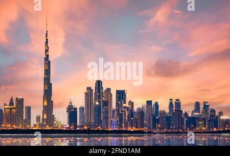 Splendida vista panoramica dello skyline illuminato di Dubai durante uno splendido tramonto. Acqua liscia e setosa che scorre in primo piano. Dubai, Emirati Arabi Uniti. Foto Stock