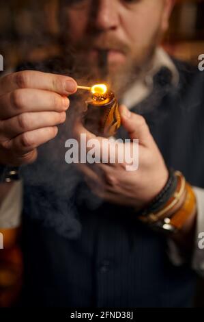 Uomo bearded luci fumando pipe con una partita Foto Stock