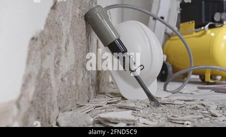 concetto di ristrutturazione della casa, muro in demolizione con macerie di gesso e attrezzature di lavoro di costruzione di protezione, casco, compressore giallo e aria pneumatica h Foto Stock