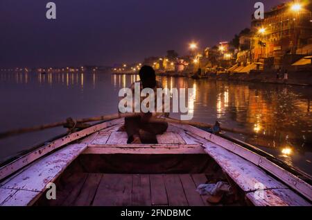 Varanasi, India - 01 novembre 2016: Un uomo che remi una pagaia di legno su una barca prima dell'alba nel fiume ganges contro loca illuminata città Santa varanasi Foto Stock