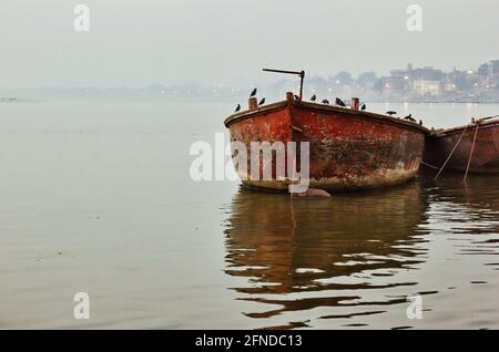 Mazzo di uccelli seduti su una vecchia barca arrugginita contro nebbia nebbia nebbia orizzonte in Varanasi situato in uno stato di Utttar pradesh, India Foto Stock