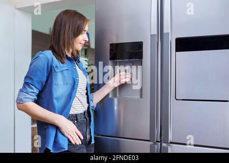 Erogatore di acqua, donna che prende l'acqua fredda in vetro dal frigorifero domestico Foto Stock