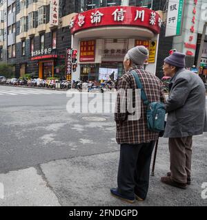 Due anziani signori attendono un semaforo per attraversare un incrocio a Shanghai, Cina Foto Stock