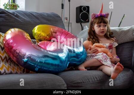 Una ragazza cute del bambino seduta su UN divano con UN Mongolfiera colorata e una bambola Foto Stock