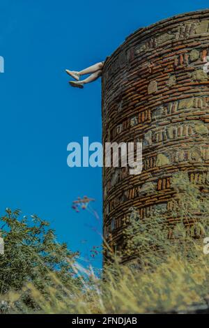 Le gambe delle donne che escono nell'aria dall'alto antica parete del castello - erbacce fuori fuoco in primo piano - Tbilisi Georgia Foto Stock