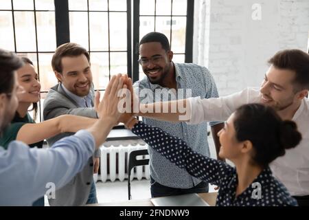 Eccitati compagni di squadra millenari che si uniscono alle mani per offrire five di alto livello Foto Stock