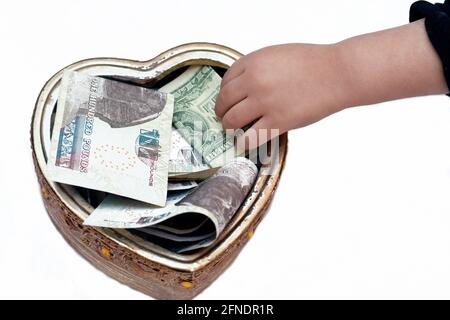 un bambino che mette 1 dollaro in una scatola di donazione con una forma del cuore, raccogliendo i soldi per la carità, aiutando la gente povera, una scatola con le valute multiple, donat Foto Stock